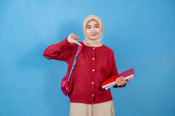 A young woman wearing a red sweater and a white skirt is holding a red book and a red backpack. She is smiling and giving a thumbs down gesture. Concept of casualness and nonchalance