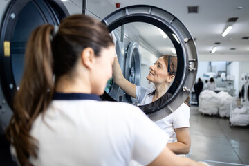 Female workers sorting dirty laundry and loading washing machine in dry cleaning service.