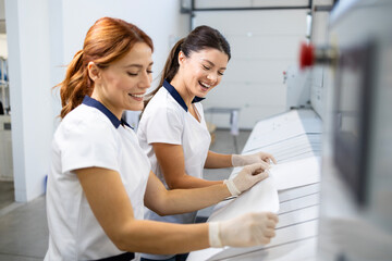Fototapeta premium Beautiful laundry workers preparing bedsheets and pillowcases for industrial ironing machine.