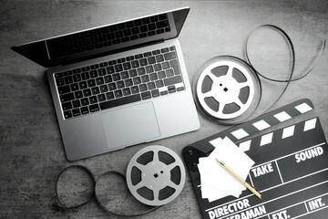 Flat lay composition with movie clapper, film reels and laptop on grey textured table