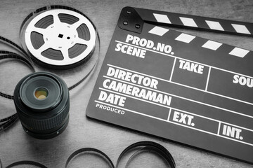 Movie clapper, film reel and camera lens on grey textured table