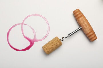 Corkscrew, cork and red wine stains on white background, top view