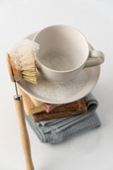 Stack of sponges, rags, natural soap and clean white cup with brush on white background. Eco-friendly dishwashing concept
