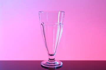 One empty glass on table against color background