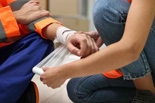 First aid. Woman putting bandage on her colleague's injured wrist after work accident indoors, closeup