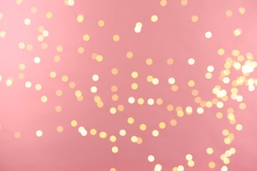 Blurred view of golden lights on pink background. Bokeh effect