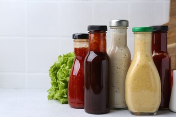 Tasty sauces in glass bottles on white table, closeup. Space for text