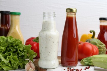 Tasty sauces in glass bottles and fresh products on white wooden table, closeup