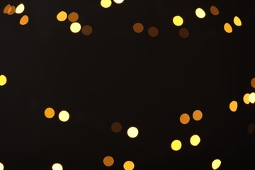 Blurred view of golden lights on black background, bokeh effect