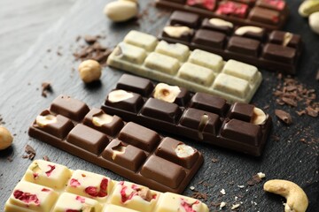 Different tasty chocolate bars with nuts and freeze dried raspberry on black table, closeup