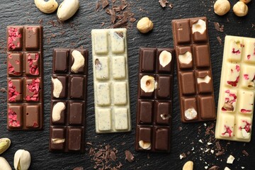 Different tasty chocolate bars with nuts and freeze dried raspberry on black table, flat lay