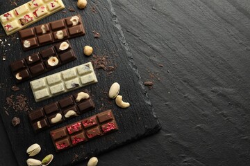 Different tasty chocolate bars with nuts and freeze dried raspberry on black table, flat lay. Space for text