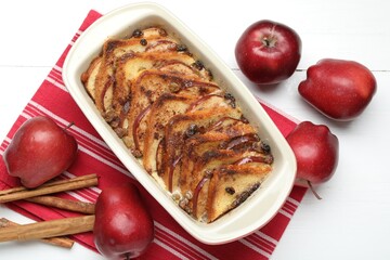 Delicious bread pudding in baking dish and fresh apples on white wooden table, flat lay