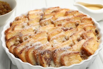 Delicious bread pudding with raisins and powdered sugar on white wooden table, closeup