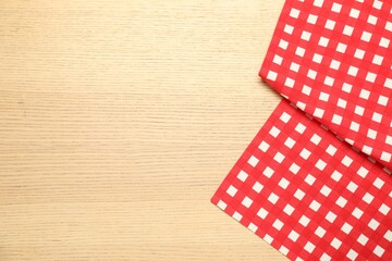 Obraz premium Red checkered tablecloth on wooden background, top view. Space for text