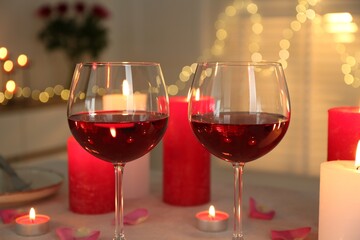 Romantic place setting with red wine, burning candles and petals on table against blurred lights, closeup
