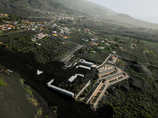 Aerial shot of modern L-shaped building amidst black lava fields, contrasting with green hills....