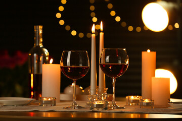 Romantic table setting with red wine and burning candles against blurred lights