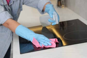 Woman using cleaning product while wiping induction cooktop with rag in kitchen, closeup