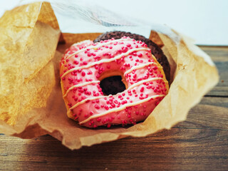 A pink donut with sprinkles on top is sitting in a paper bag. The donut is placed on a wooden...