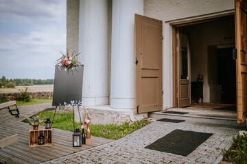 Outdoor wedding decoration near a church entrance with flowers, lanterns, and a blackboard sign, creating a rustic and elegant atmosphere.