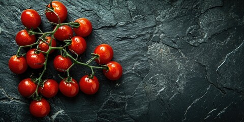 Fresh vine-ripened cherry tomatoes in vibrant red hues arranged artistically on a textured black stone surface with ample copy space on the right.