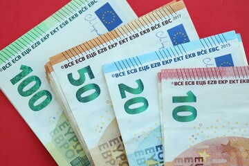 Big amount of one hundred, twenty, ten and fifty euro money bills on red background