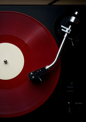 A retro and minimalist close-up of a red vinyl record on a turntable, featuring a white center label and a black tonearm positioned over the grooves.