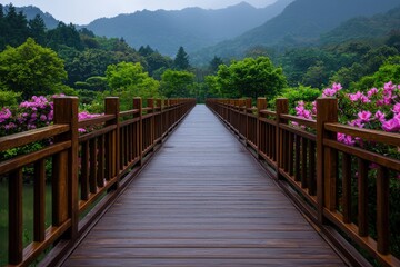 Fototapeta premium A serene wooden bridge leads through lush greenery and vibrant flowers, framed by misty mountains in the background.