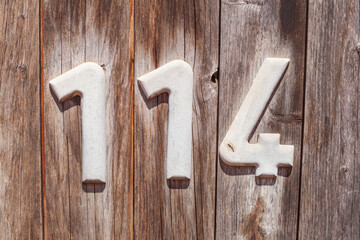 Weisses Hausnummernschild Nummer 114 auf einer Braunen Holzwand, Deutschland