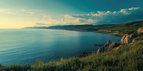 Fototapeta premium Coastal landscape at sunset featuring calm blue waters, green hills, and soft clouds illuminated by warm golden light, creating a serene atmosphere.