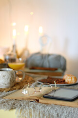 Books, e-reader, tea, orange juice, fruit, snacks, yarn, blanket and lit candles on the table. Autumn or winter hygge at home. Selective focus.