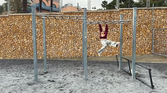 Young girl wearing christmas outfit having fun moving forward on monkey bars at a playground. Wide shot