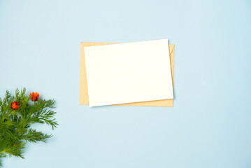 Paper blank sheet with flowers on blue background. Greeting card. Space for text. Flat lay, top view.