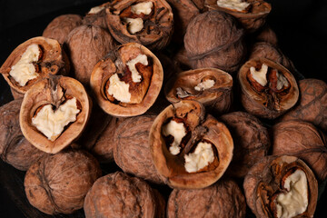 Peeled and whole walnuts lie on a glass plate. Black background.