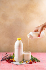 Woman pouring kefir or yogurt into glass with berries and herbs on pink table