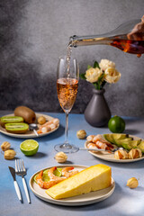 Pouring rose wine into glass with cheese, shrimp, and fruits on table