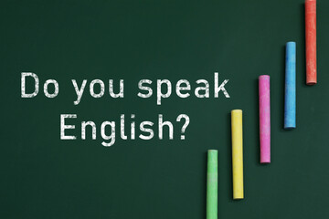Do You Speak English? text and pieces of colorful chalk on greenboard, top view. Language course