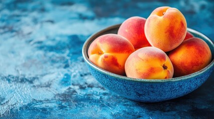 Ripe juicy peaches in a textured blue bowl on a vibrant blue table with ample empty space for text or design elements