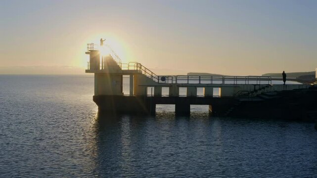Aerial pan of Blackrock diving board silhouetted at sunset. Galway, Ireland