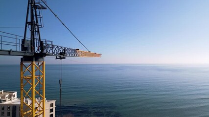 A tower crane stretches over the serene blue sea on a sunny day. A perfect view of construction meeting nature, showcasing progress and harmony by the coastline