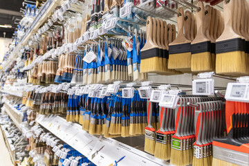 wide selection of paintbrushes on display in a hardware store aisle with colorful handles and price...