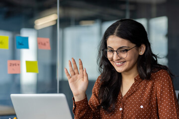 Video call, young woman smiling waving hand greeting colleagues and partners. Office worker using...