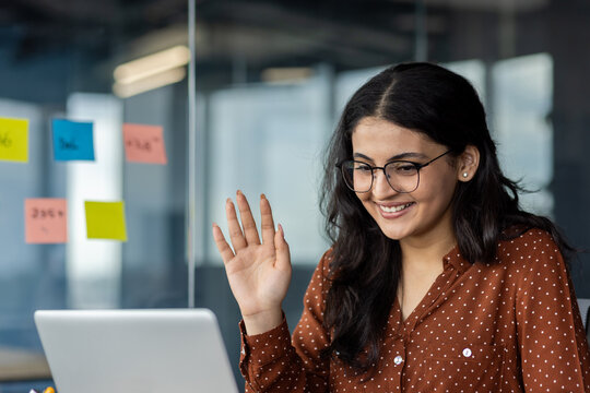 Video call, young woman smiling waving hand greeting colleagues and partners. Office worker using laptop for online communication, business conference, and meeting. Successful businesswoman close up.