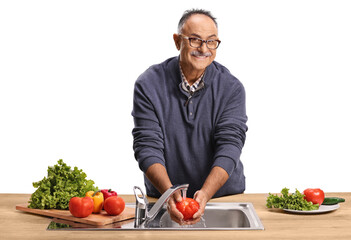 Mature man washing a tomator in a kitchen sink