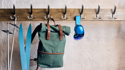 Blue skis, green backpack, and ski goggles displayed together, emphasizing creative winter outdoor experiences and cozy travel spirit. Concept of cozy winter, style, aesthetic, travelling and relax.