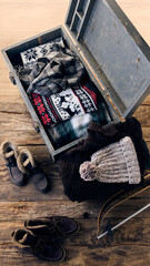 Top view of vintage chest filled with winter essentials, including festive sweaters and scarves, surrounded by warm boots and skis, representing cozy holiday vibes. Concept of travelling and relax.