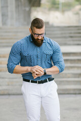 Strong bearded hipster businessman walking and looking at the time outside. Male modern business fashion and urban lifestyle.