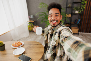 Close up young man of African American ethnicity wears grey casual clothes do selfie shot on mobile cell phone sitting alone at table in coffee shop cafe relax rest in restaurant in free time indoors.