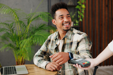 Young man wears casual clothes hold wireless modern bank payment terminal to process acquire smart...